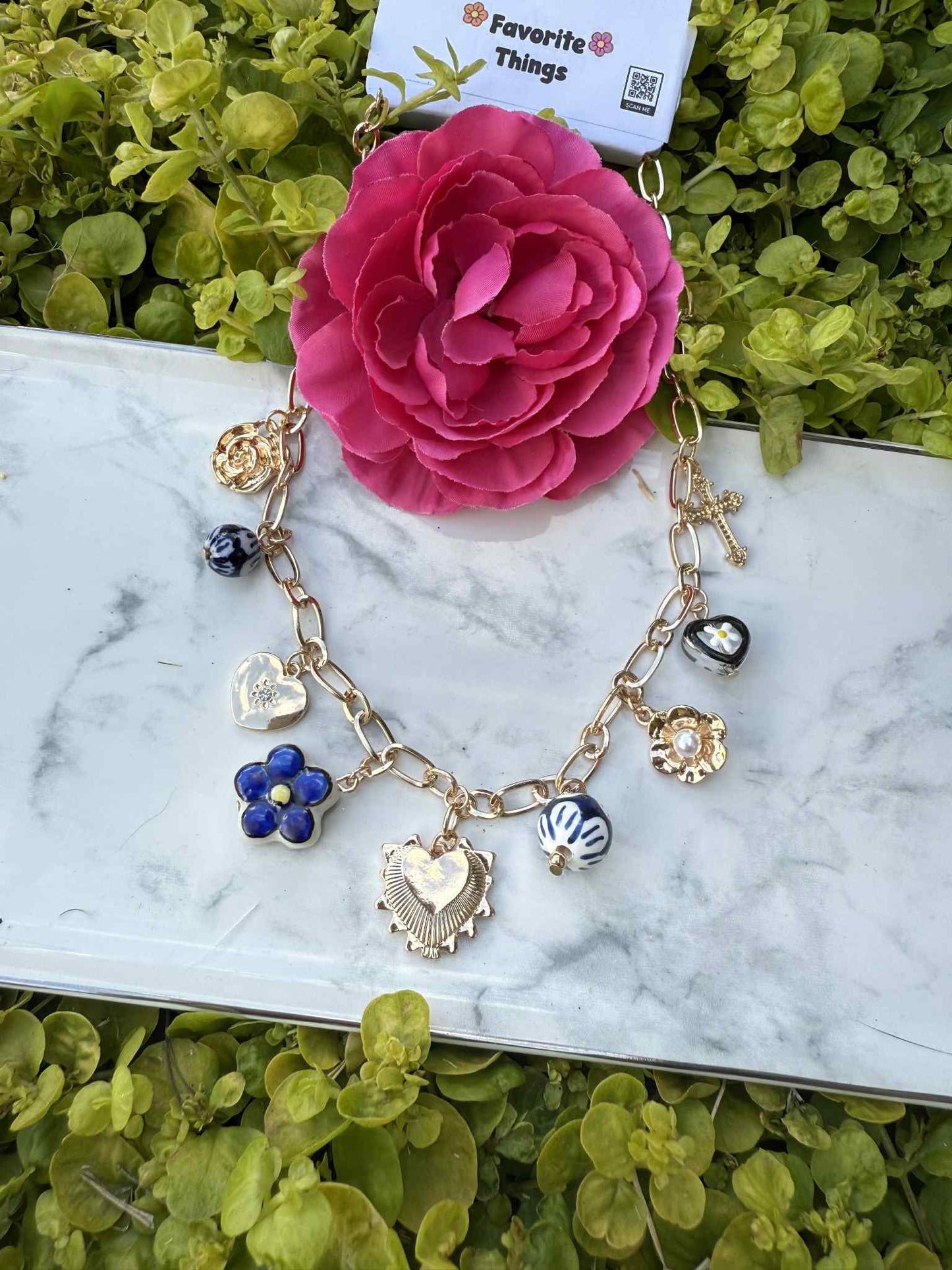 Bracelet with charms on a marble surface with a pink flower in the background