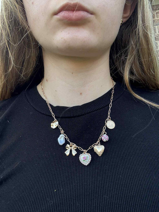 Necklace with pink ceramic charms and gold heart and bows on black background