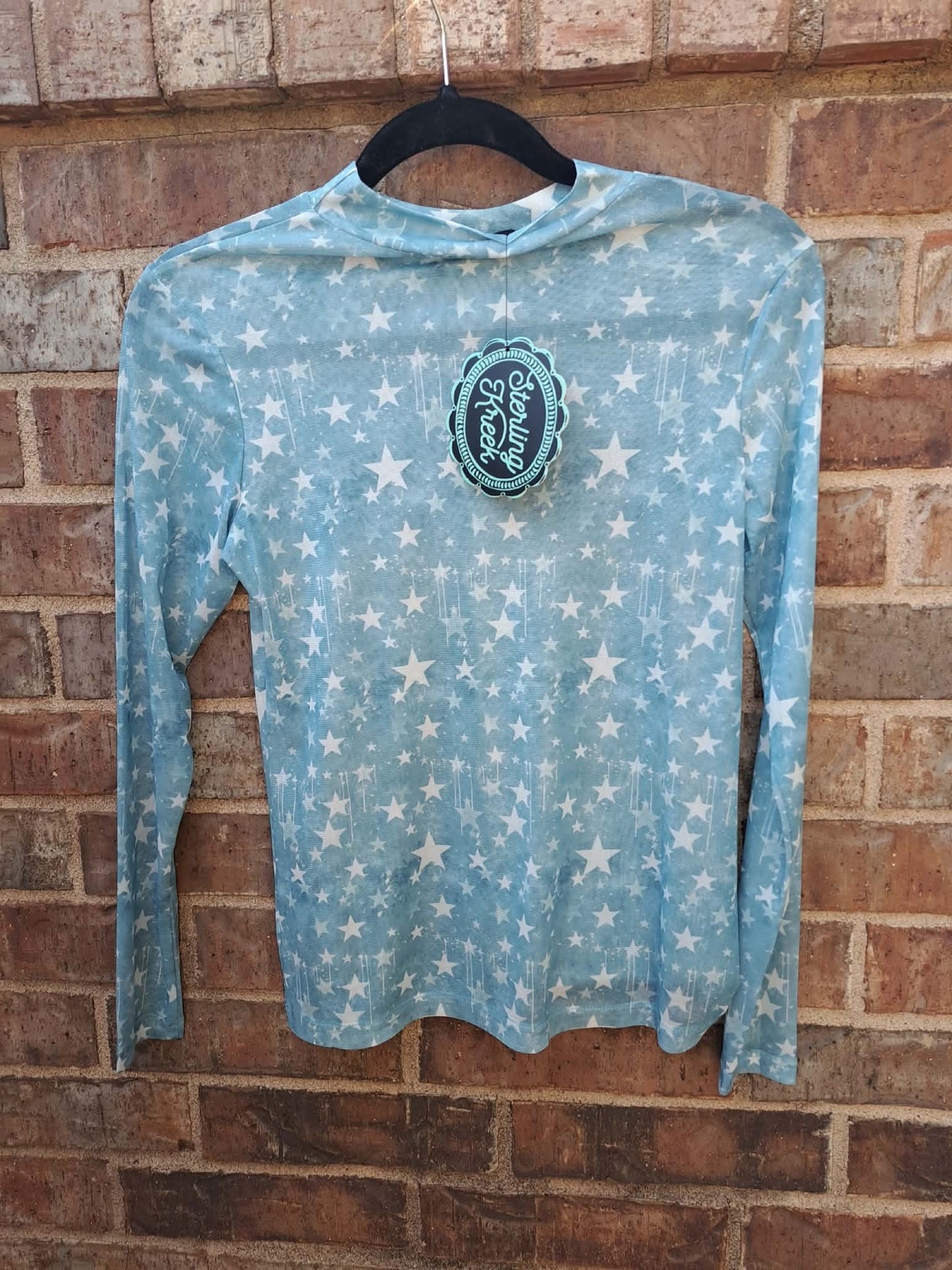 Blue long-sleeve shirt with star pattern and logo on a hanger against a brick wall.