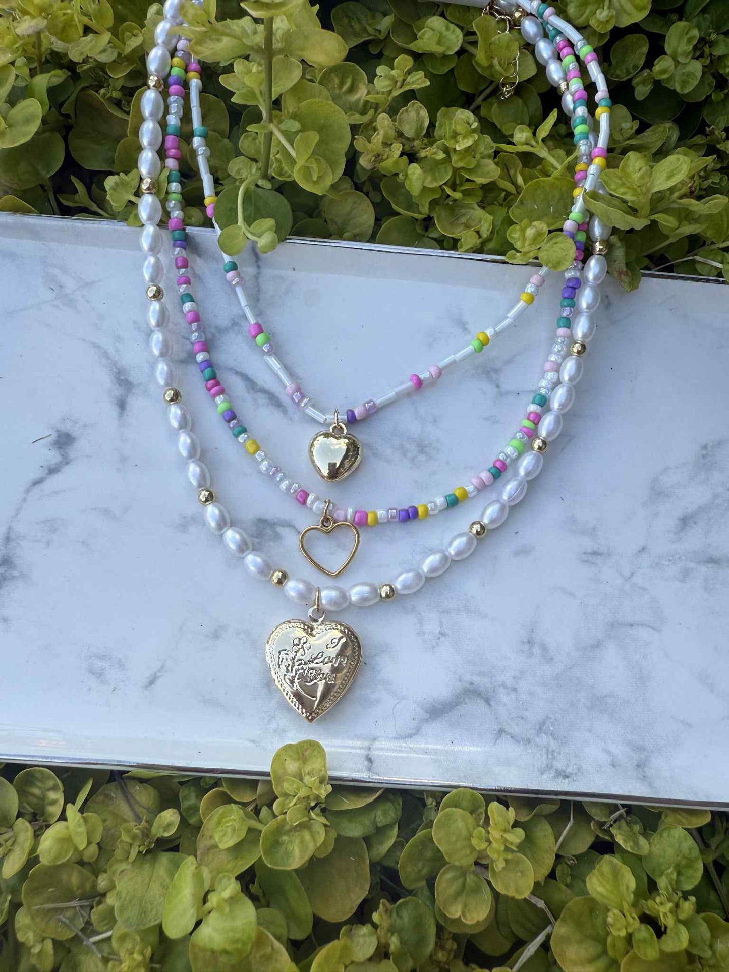 Pearl and bead necklace with Gold heart charms on white marble background, front