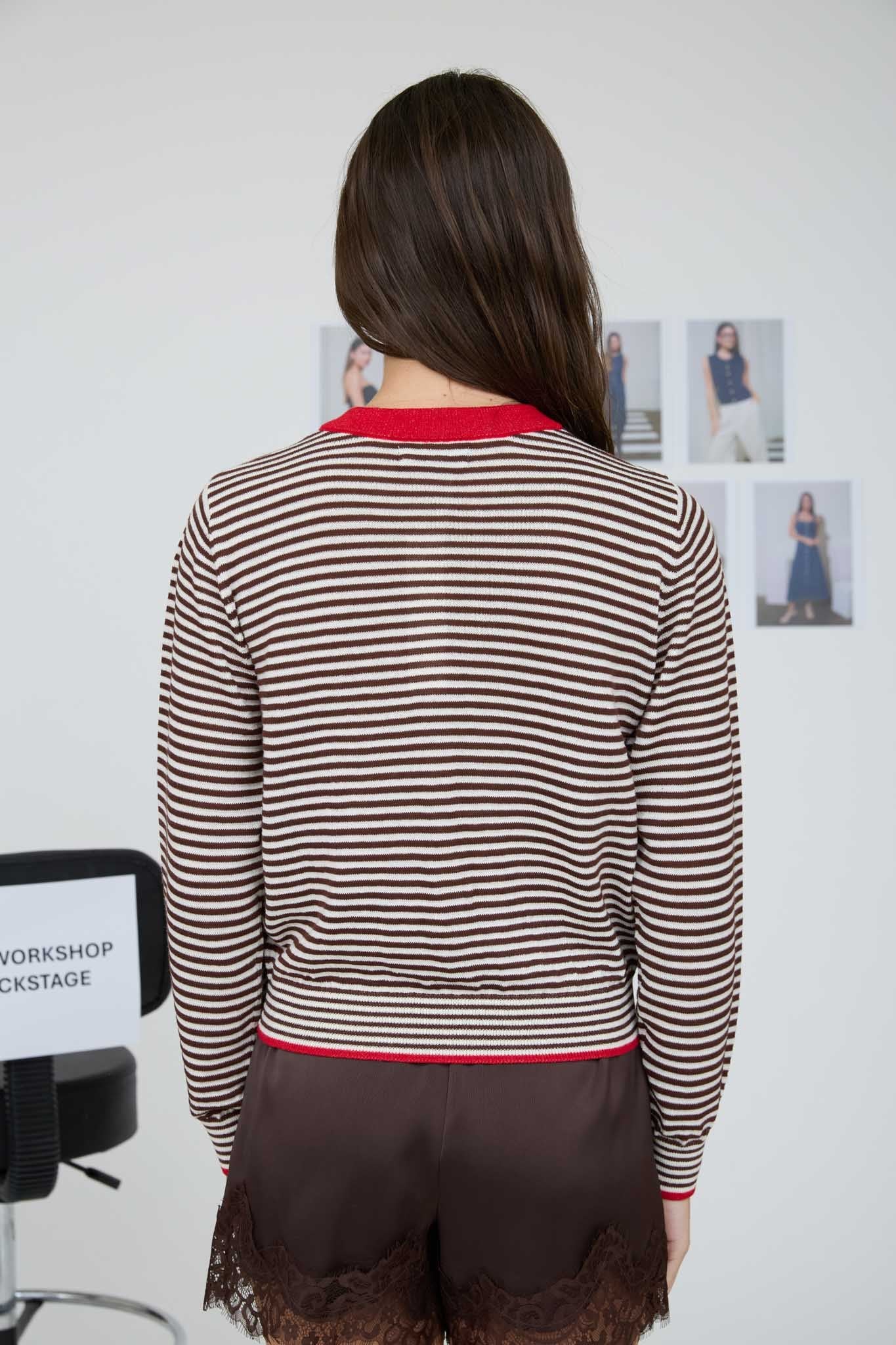 Woman wearing a striped sweater and black shorts in front of a white wall with photos.