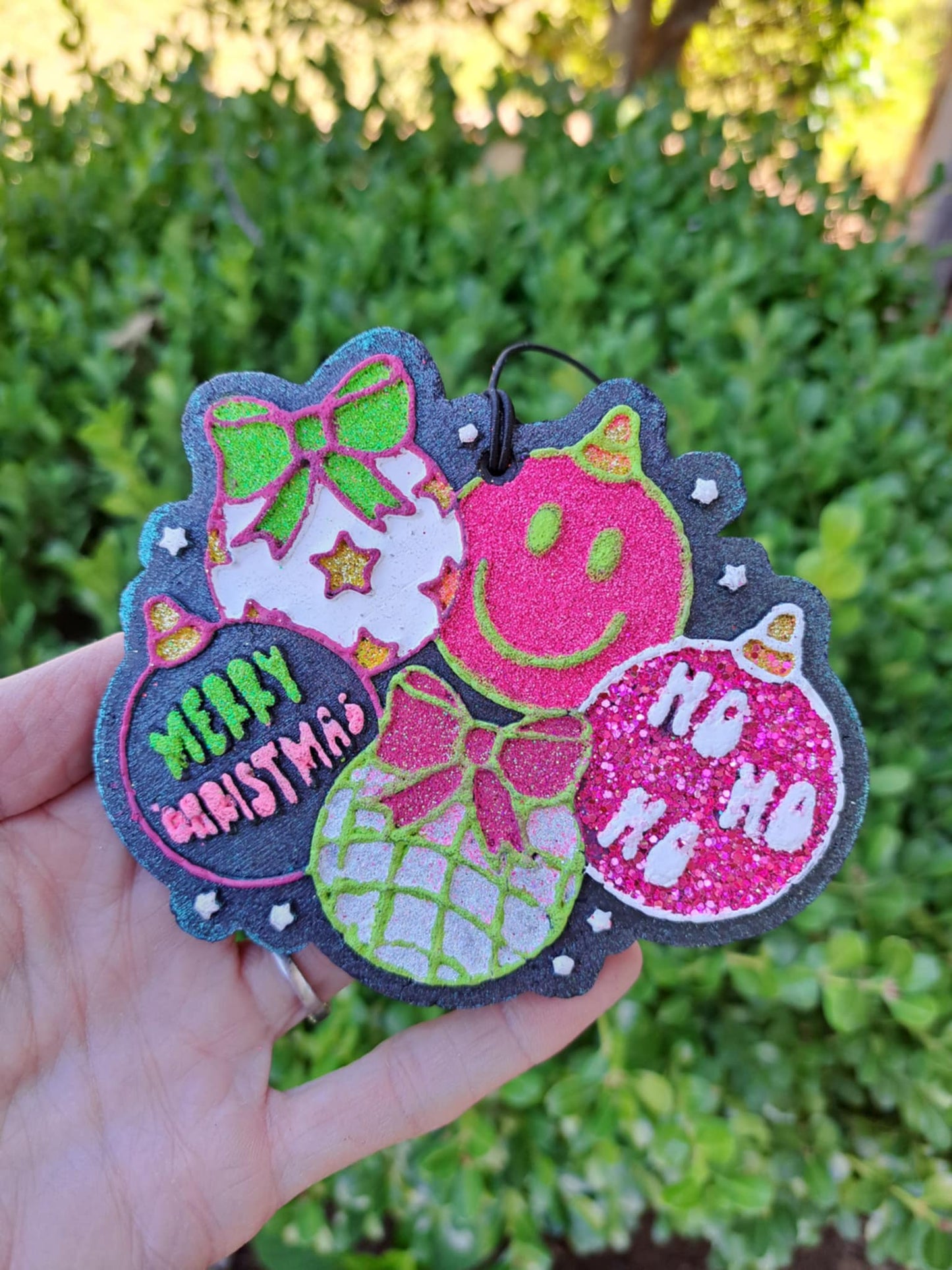 Decorative Christmas ornament freshie with colorful designs held by a hand against a green bush background.