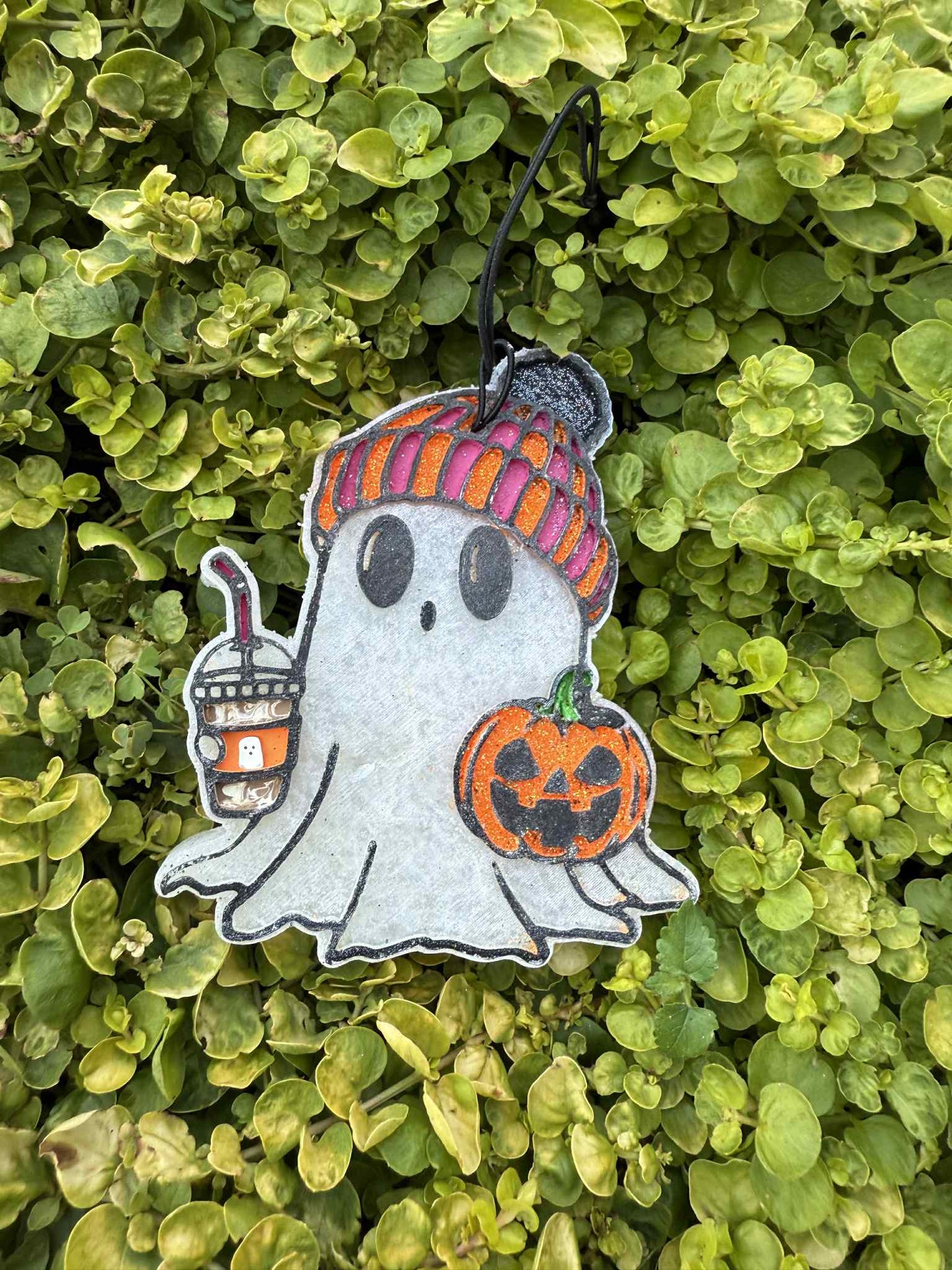 Ghost freshie wearing stocking cap and holding drink and pumpkin. Greenery background.