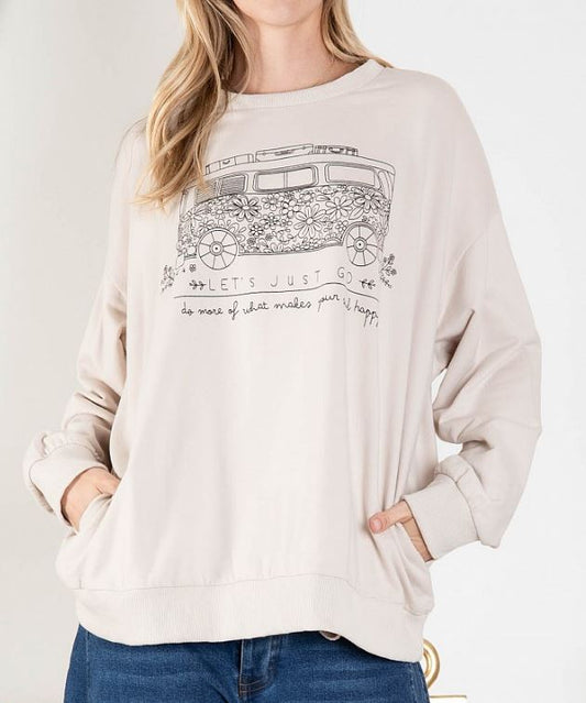 A woman wearing a beige oversized knit pullover with a flower bus print. She has her hands in her pockets and is posing against a white background.