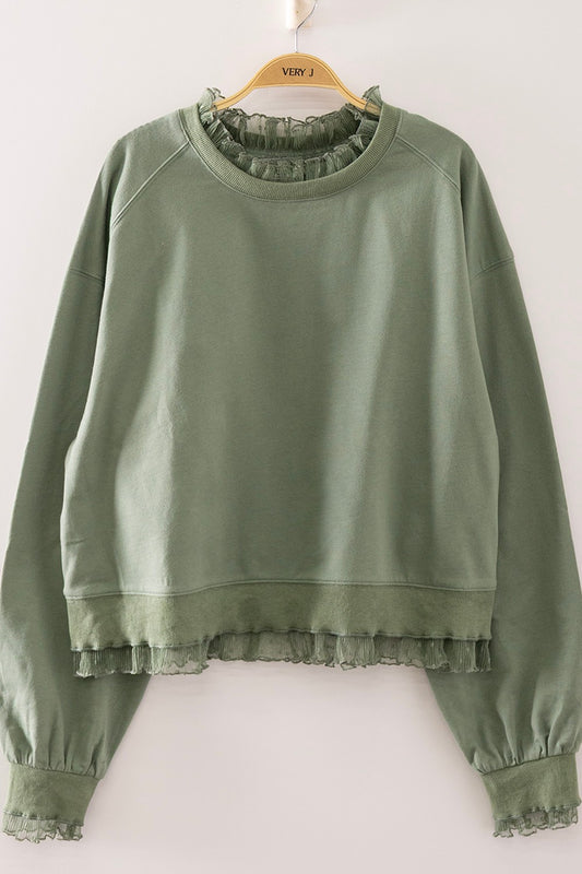 An olive green long-sleeve sweatshirt with a ruffled mock neck, ruffled hem, and ruffled cuffs, hanging on a wooden hanger against a plain white wall.