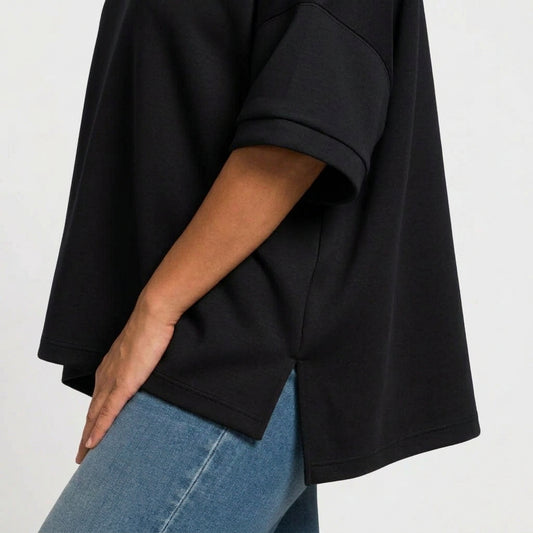 Close-up of a person wearing an oversized black short-sleeve top with blue jeans, cropped to show the side and back drape of the shirt.