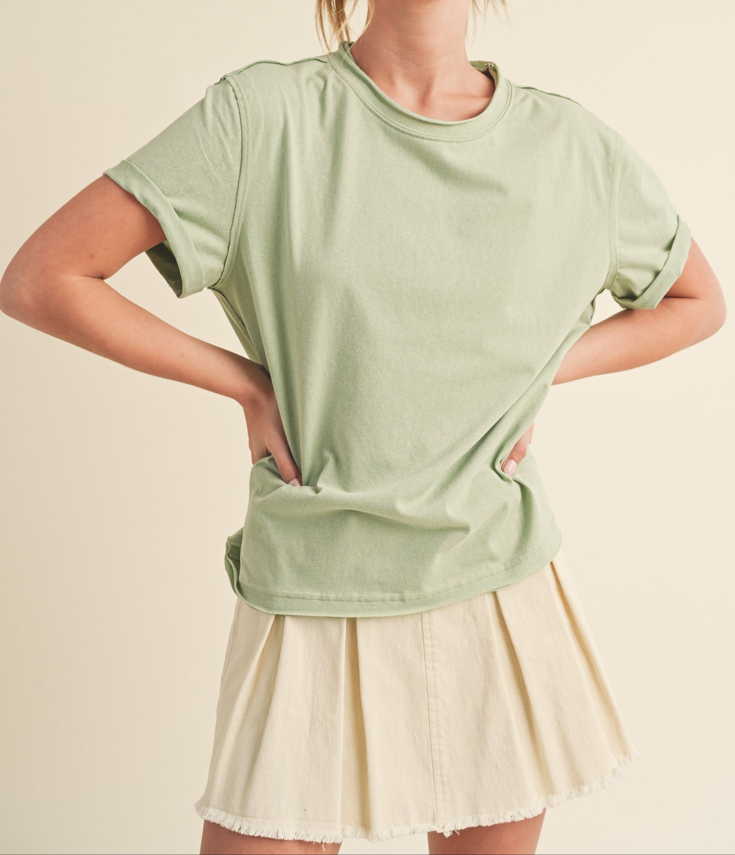 Woman wearing a light green oversized t-shirt and beige skirt on a beige background