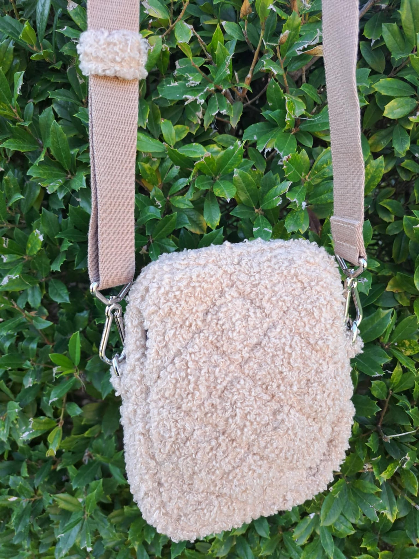 Beige textured bag with a strap against a green leafy background