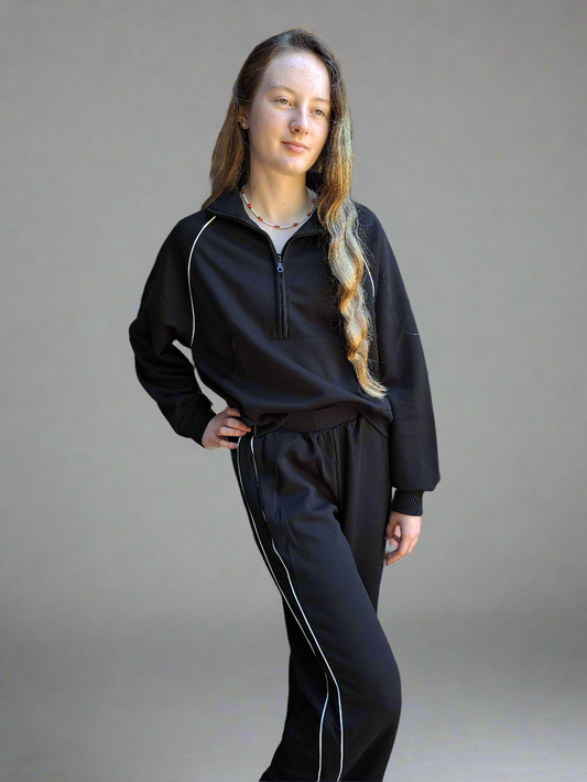 Person wearing a black tracksuit with white piping on a gray background