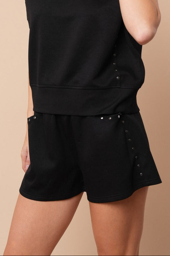 side view of black knit shorts with stud trim on woman. beige background