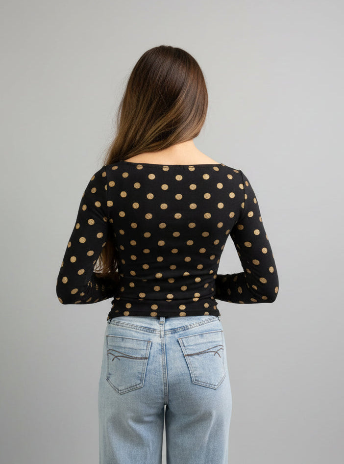 back view of a woman wearing a black polka dot top and jeans against a neutral background