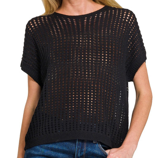 A woman wearing a black crochet knit open sweater vest paired with blue  jeans. white background