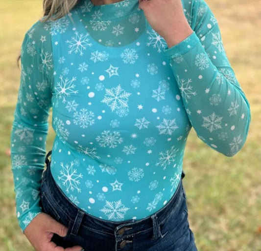 blue snowflake print mesh top and jeans on a woman with a green background