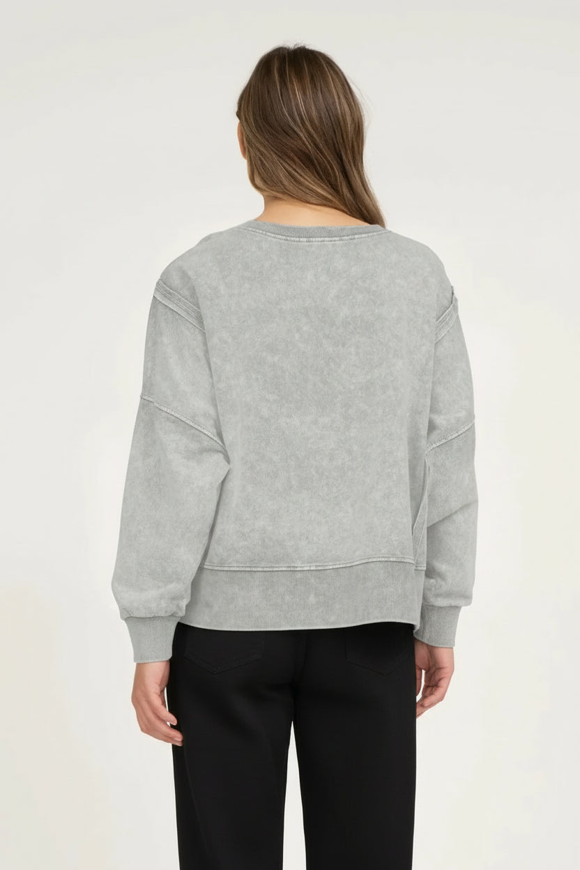 Person wearing a gray sweater and white pants on a plain background