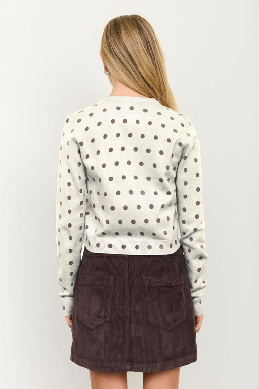 A woman viewed from the back wearing a cream long-sleeve crop top with dark brown polka dots and a dark brown corduroy mini skirt, set against a plain light gray background.