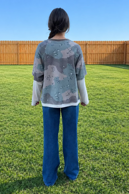 lady wearing layered camo top and jeans standing in grassy yard