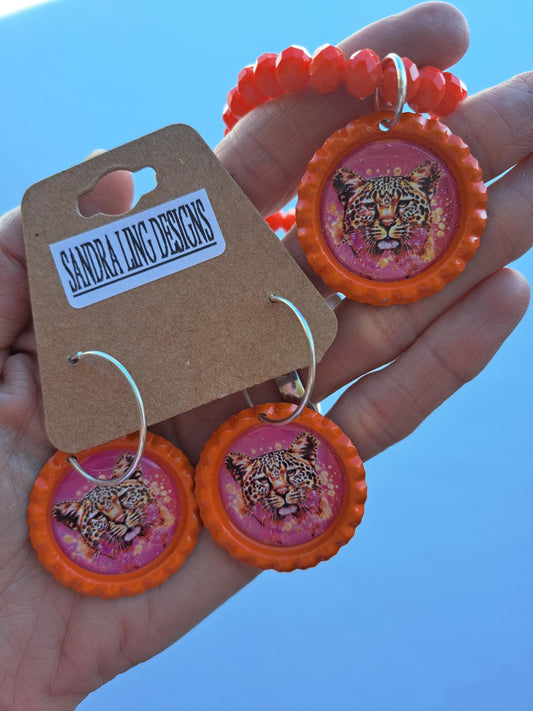 Orange earrings with tiger design held against a snowy background