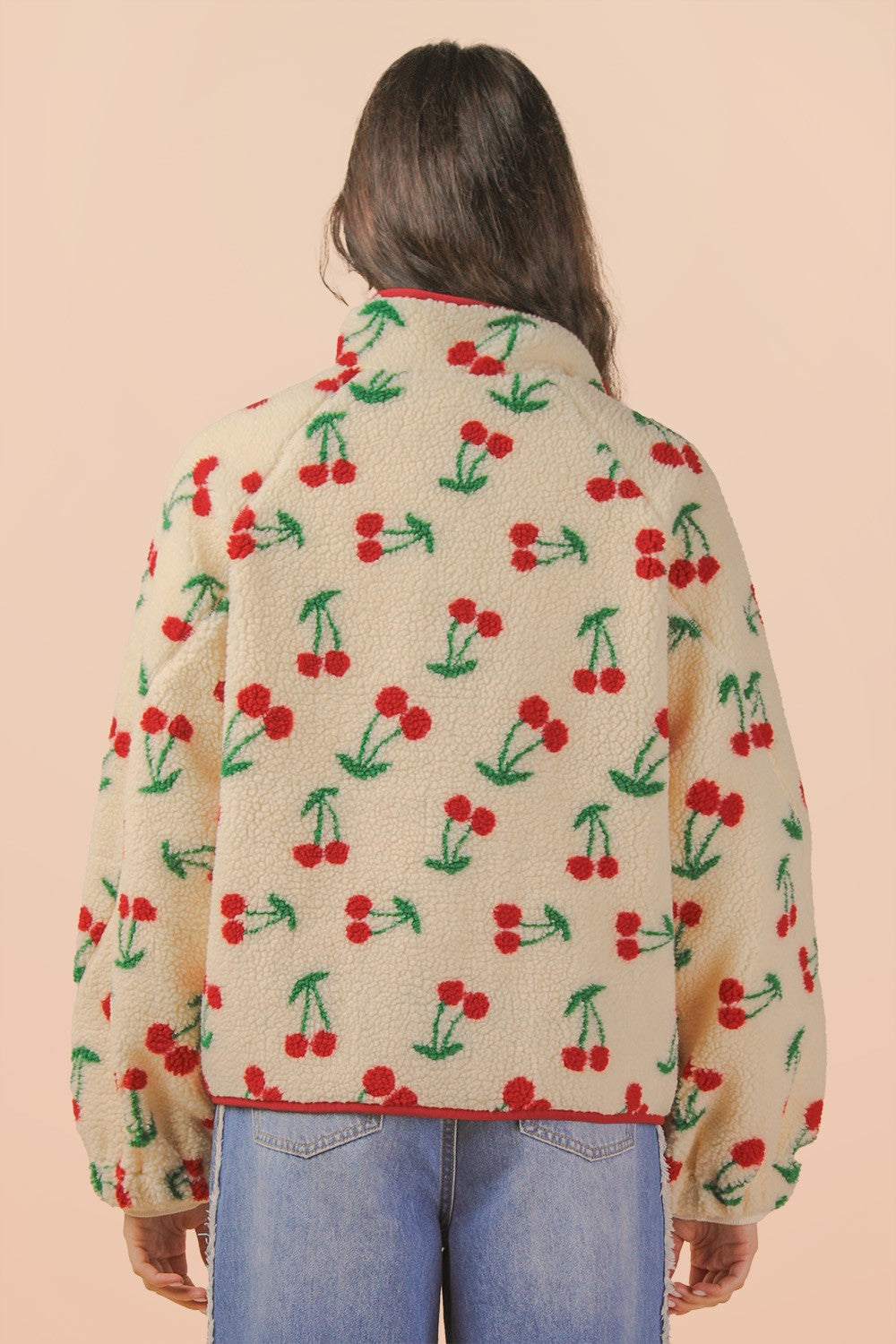 Person wearing a sweater with cherry pattern on a beige background