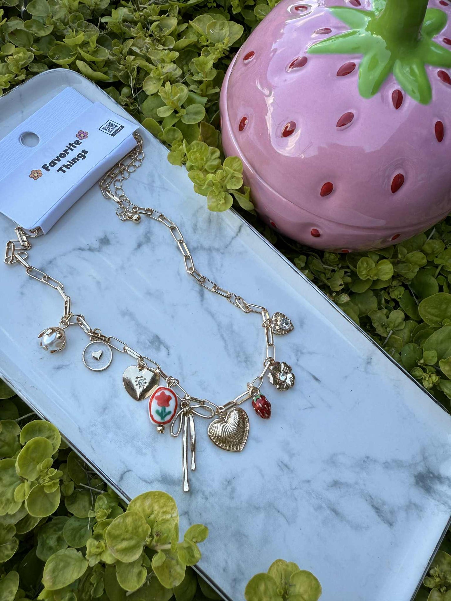 Necklace with charms on a marble surface with a strawberry-shaped container in the background.
