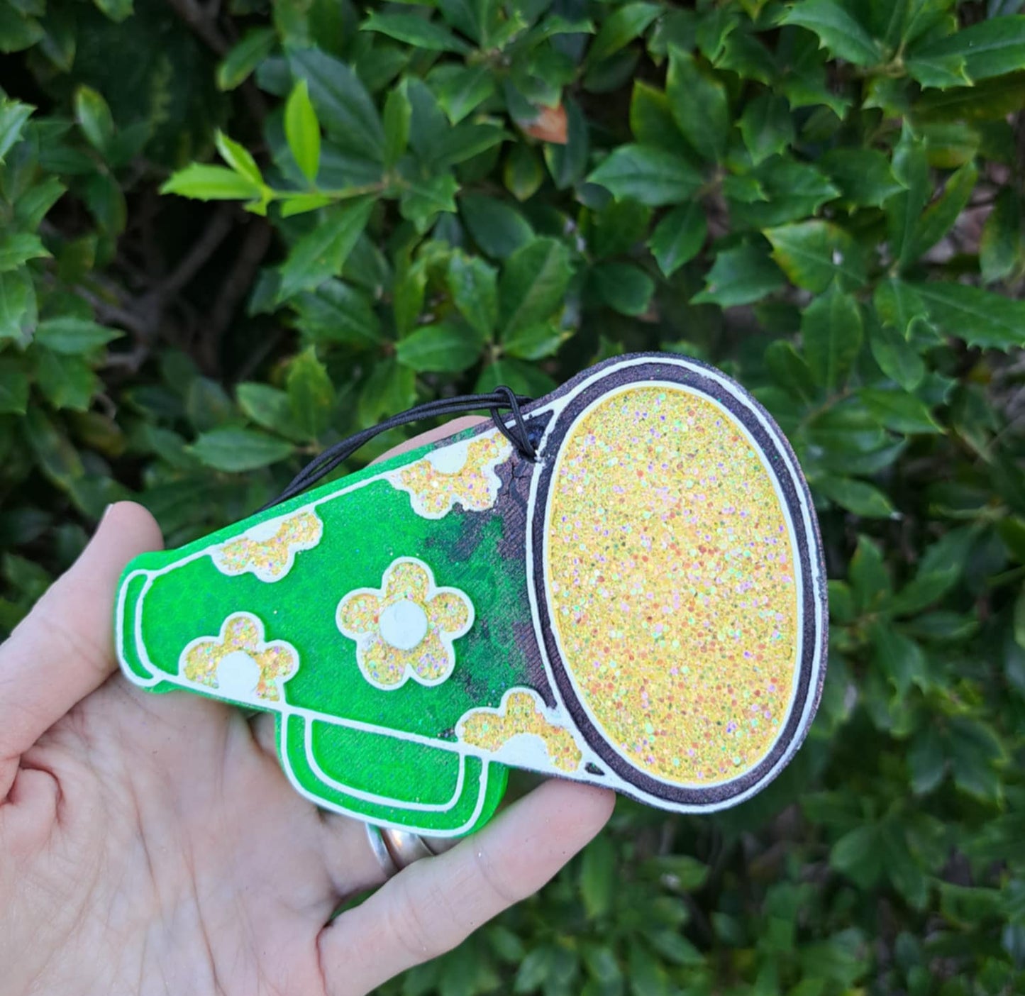 Hand holding a green and yellow megaphone against a green leafy background