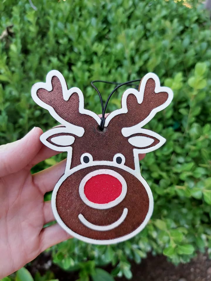 Hand holding a reindeer-shaped freshie with a red nose against a green bush background