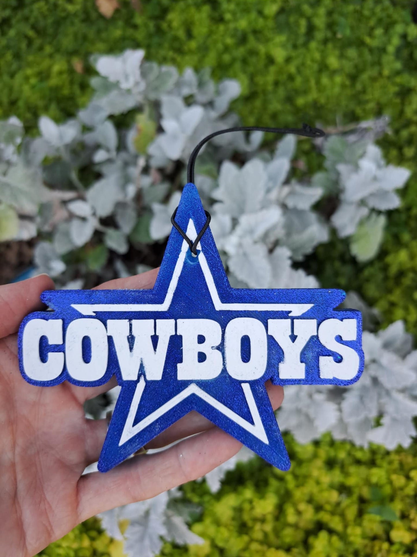 Blue star-shaped cowboy ornament held in front of green and white foliage.