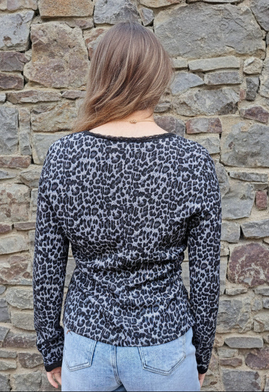 Person wearing a leopard print top and light blue jeans standing in front of a stone wall
