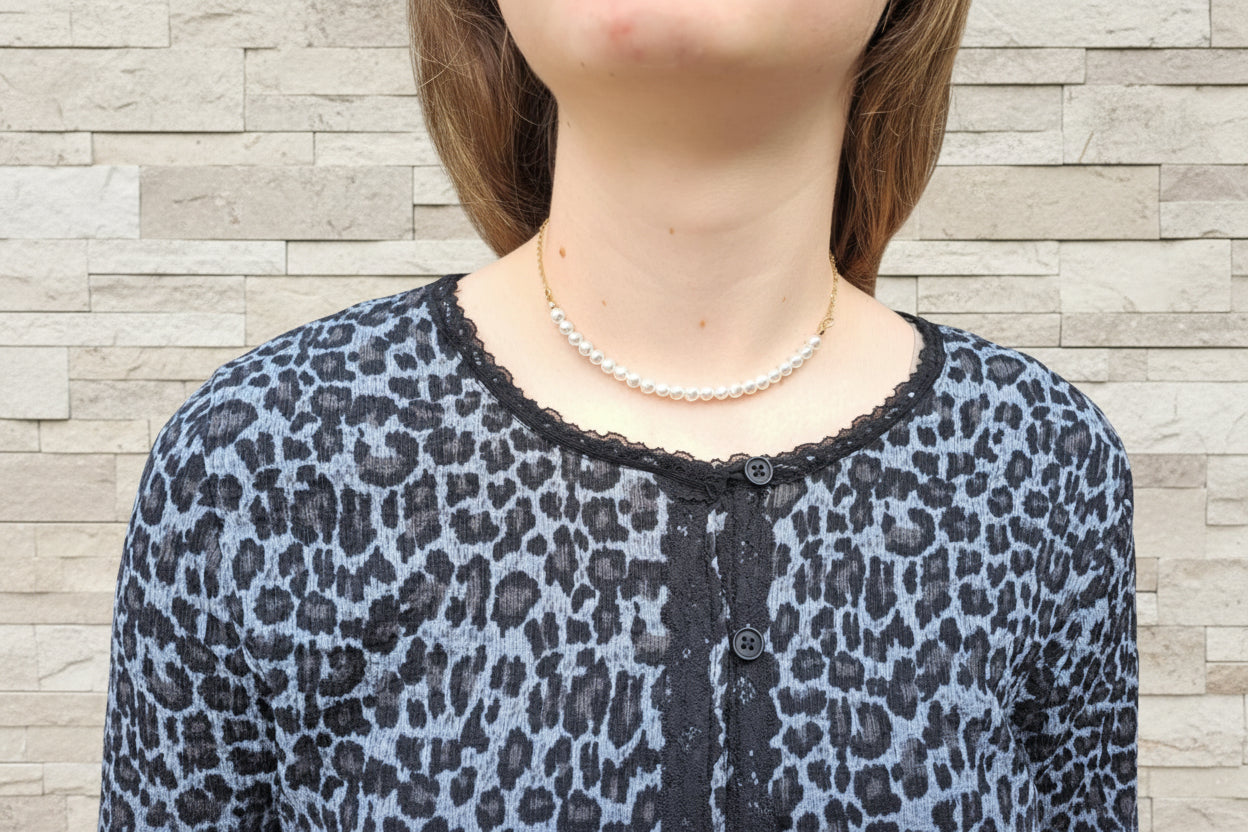 Person wearing a leopard print top with a pearl necklace, standing outdoors.