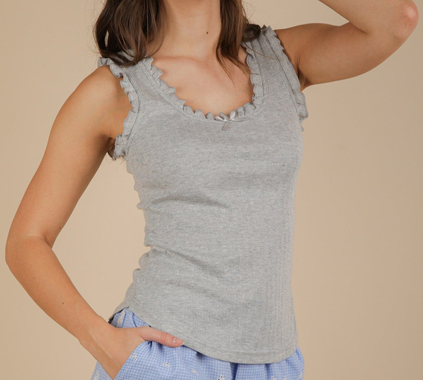 Woman wearing a gray sleeveless top and blue pants with floral patterns on a beige background