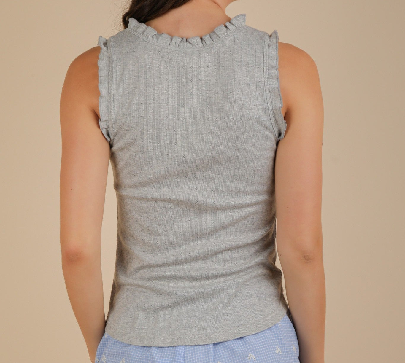 Woman wearing a gray sleeveless top with ruffled shoulders against a beige background
