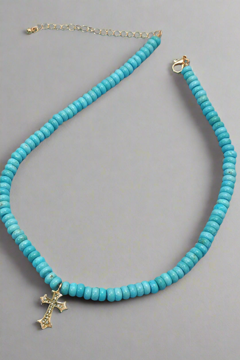 A beaded necklace with blue beads and a gold-colored cross charm, with a gold-plated lobster claw clasp.