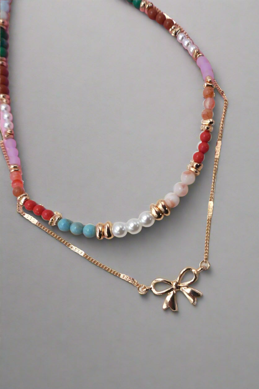 Necklace with colorful beads and bow charm on a pink background