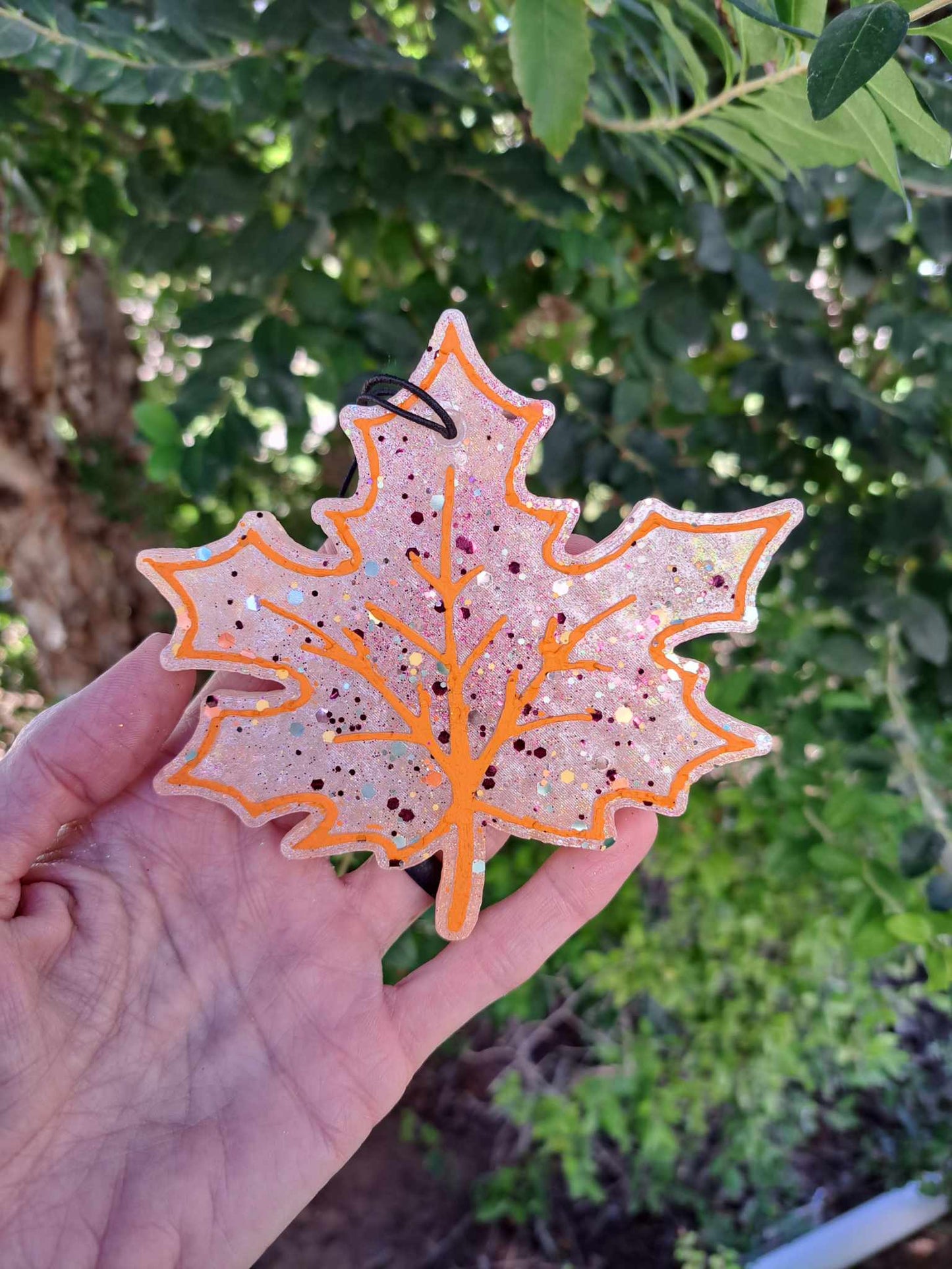Hand holding a white leaf shaped freshie with orange trim. green background