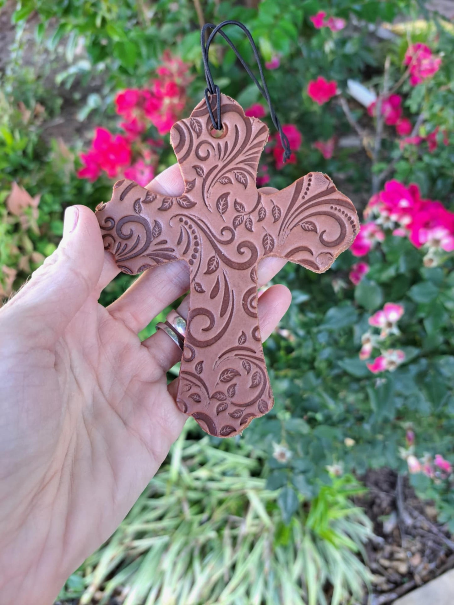 leather tooled cross freshie held in front of greenery