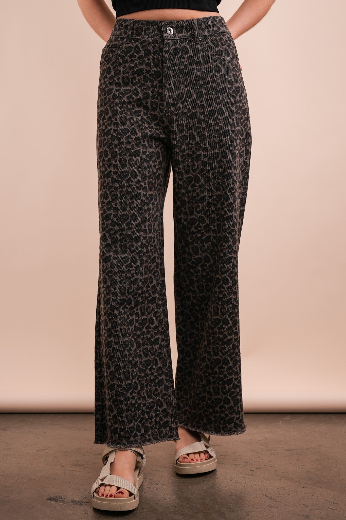 A person standing wearing leopard print straight leg crop jeans and tan sandals.