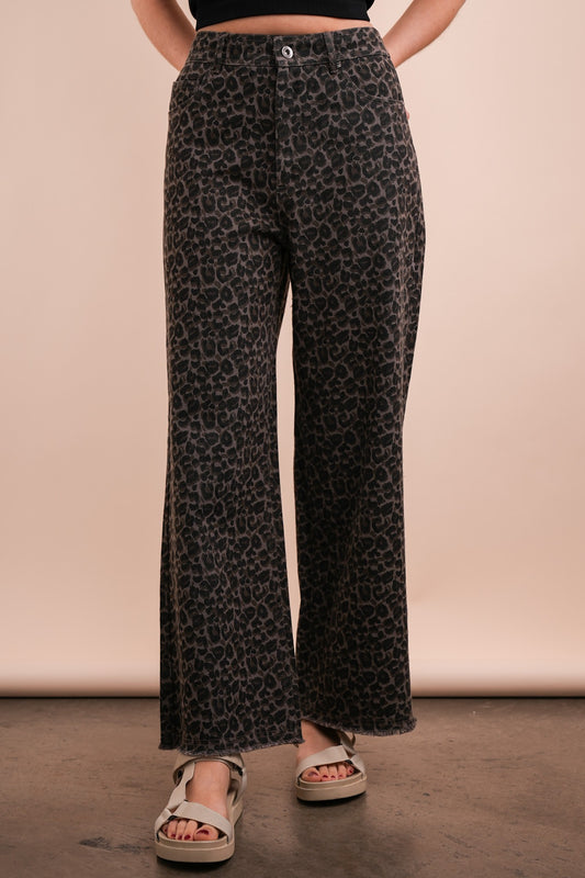 A person standing wearing leopard print straight leg crop jeans and tan sandals.