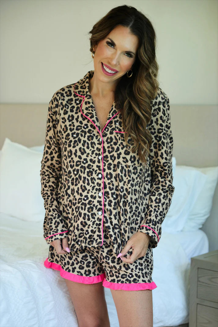 Woman wearing leopard print pajamas with pink trim in a bedroom setting.