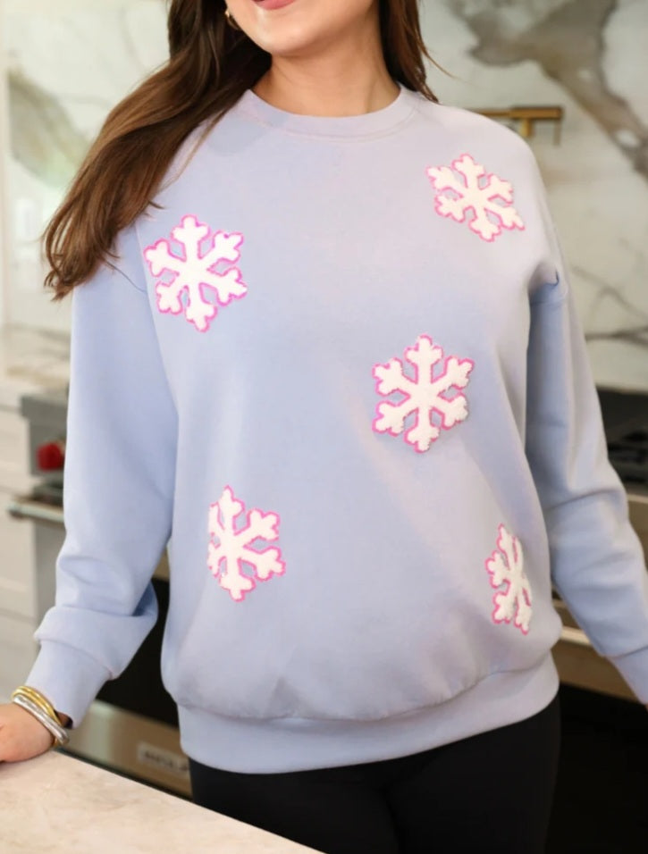 A woman wearing a blue sweatshirt with chenille snowflake patches sewn on with a pink sequin outline.