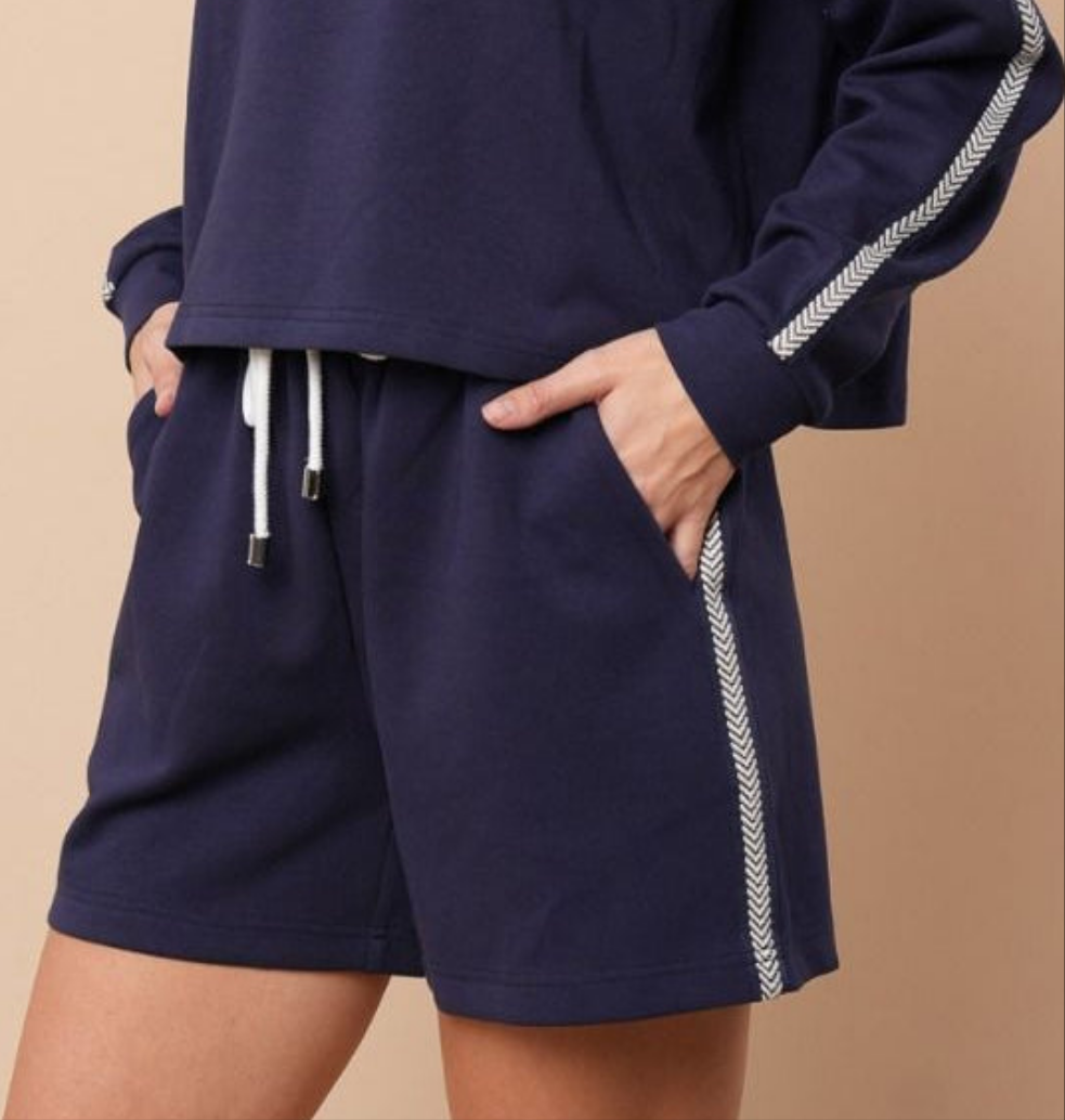 Navy knit shorts with white arrow stripe down the side on a beige background