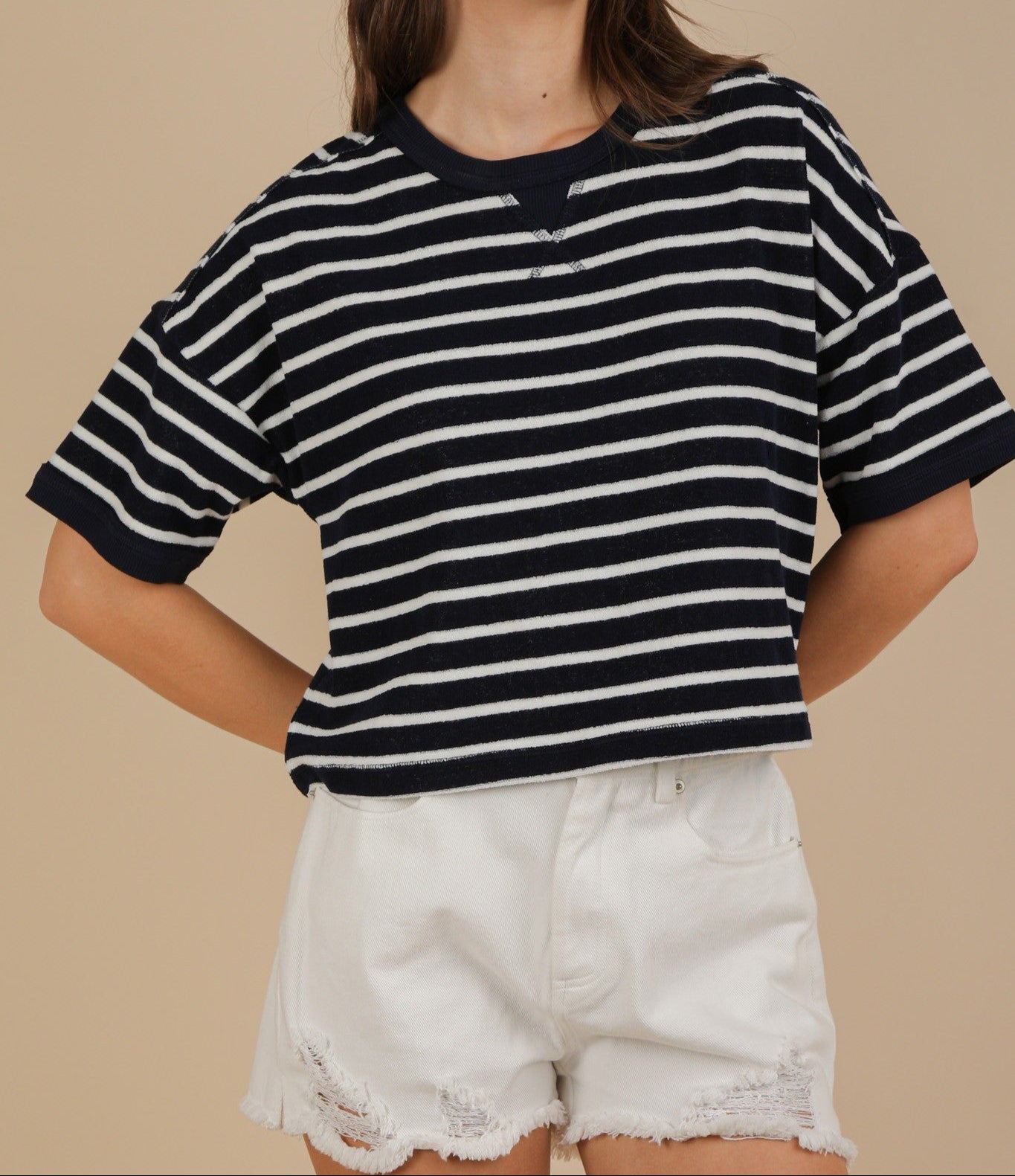 Woman wearing a navy and white striped shirt with white shorts on a beige background