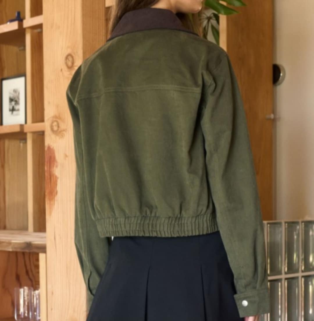 Person wearing a green jacket in an indoor setting. Back view.