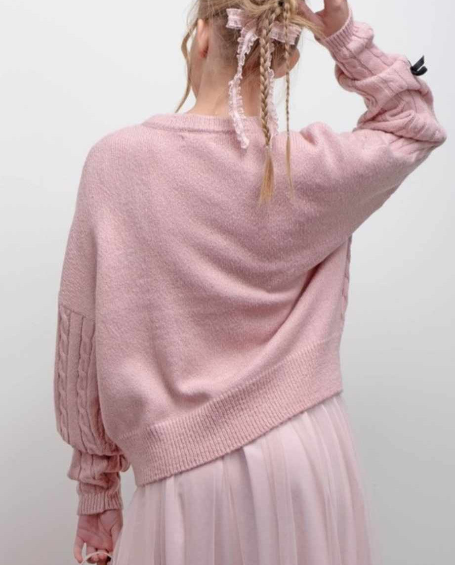 Back view of a person wearing a pink cable knit sweater on a white background