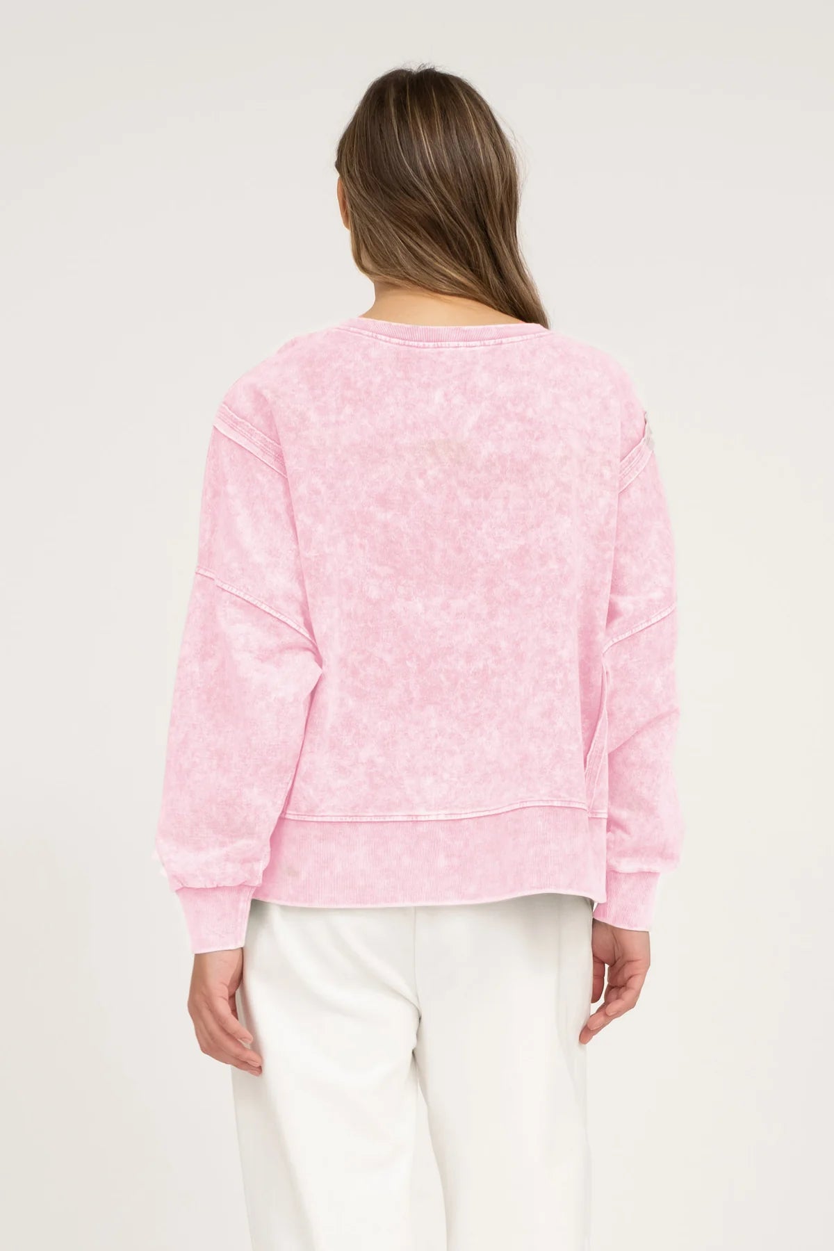 Back view of a person wearing a pink acid wash top on a neutral background.