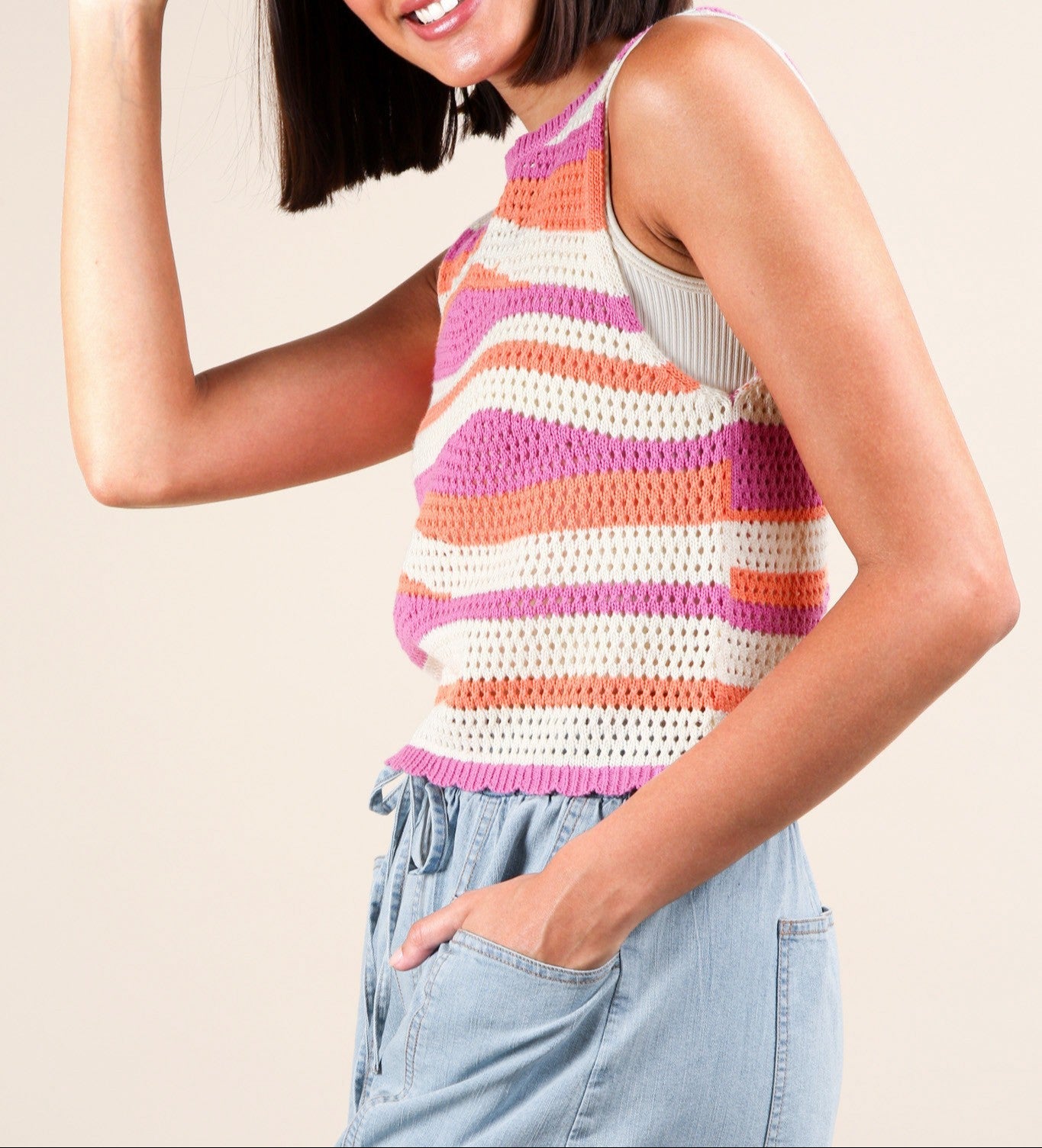 A person wearing a pink and orange stripe knit crop sweater tank top paired with light blue denim shorts.