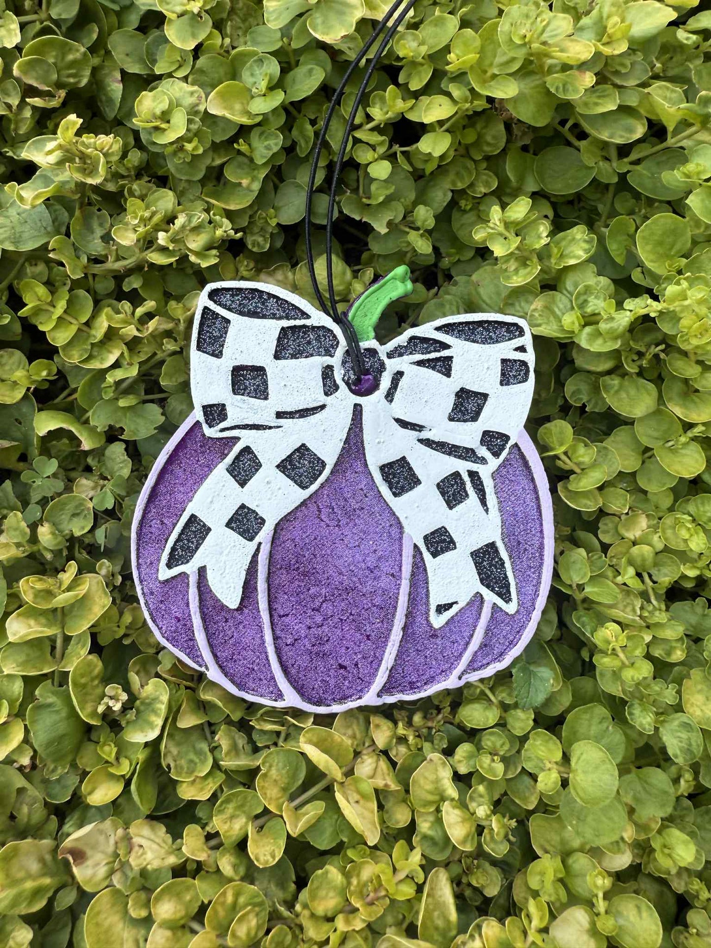 Purple pumpkin with black white checkered bow. Greenery background.
