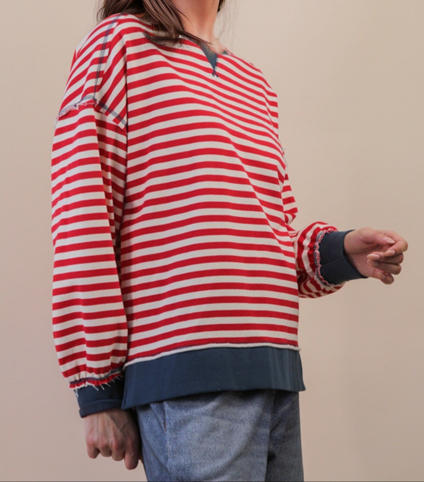 side view of red and cream top with blue trim on person wearing jeans. beige background