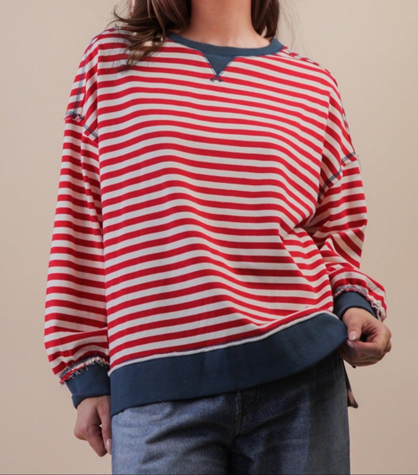 red and cream long sleeve top with blue trim on person wearing jeans. beige background