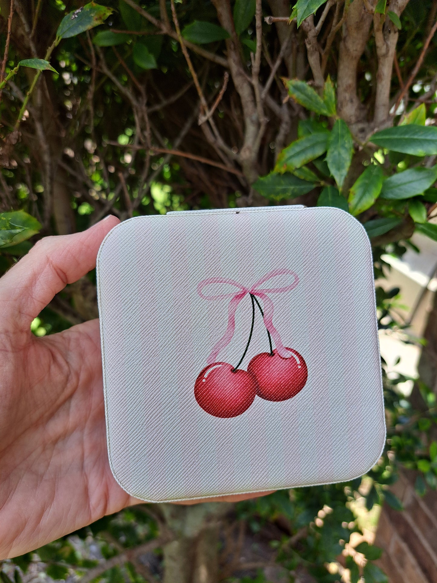 Cherries with bow printed on small pink white striped jewelry vox on green background, front