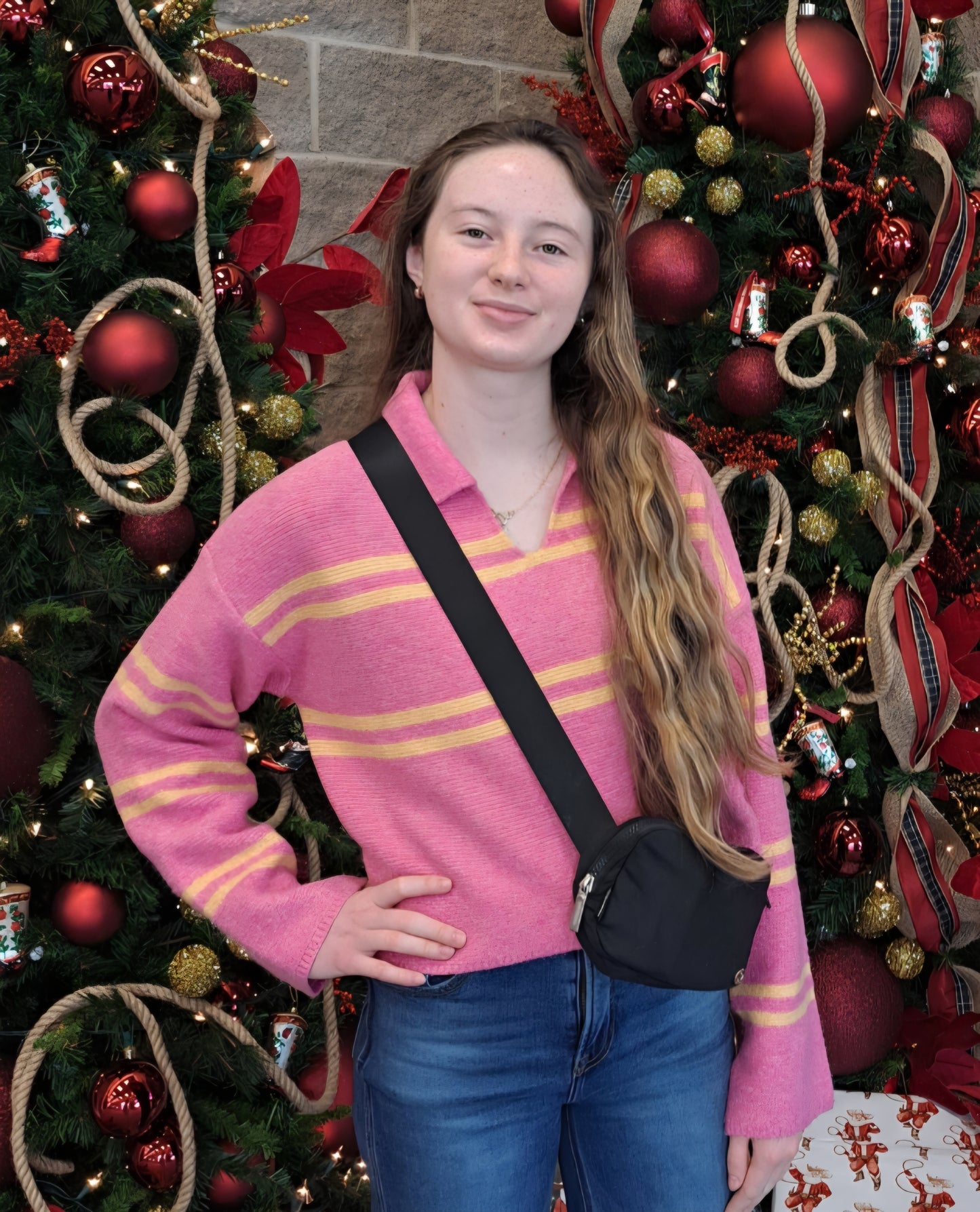 Person wearing a pink sweater with orange stripes in front of a decorated Christmas tree.