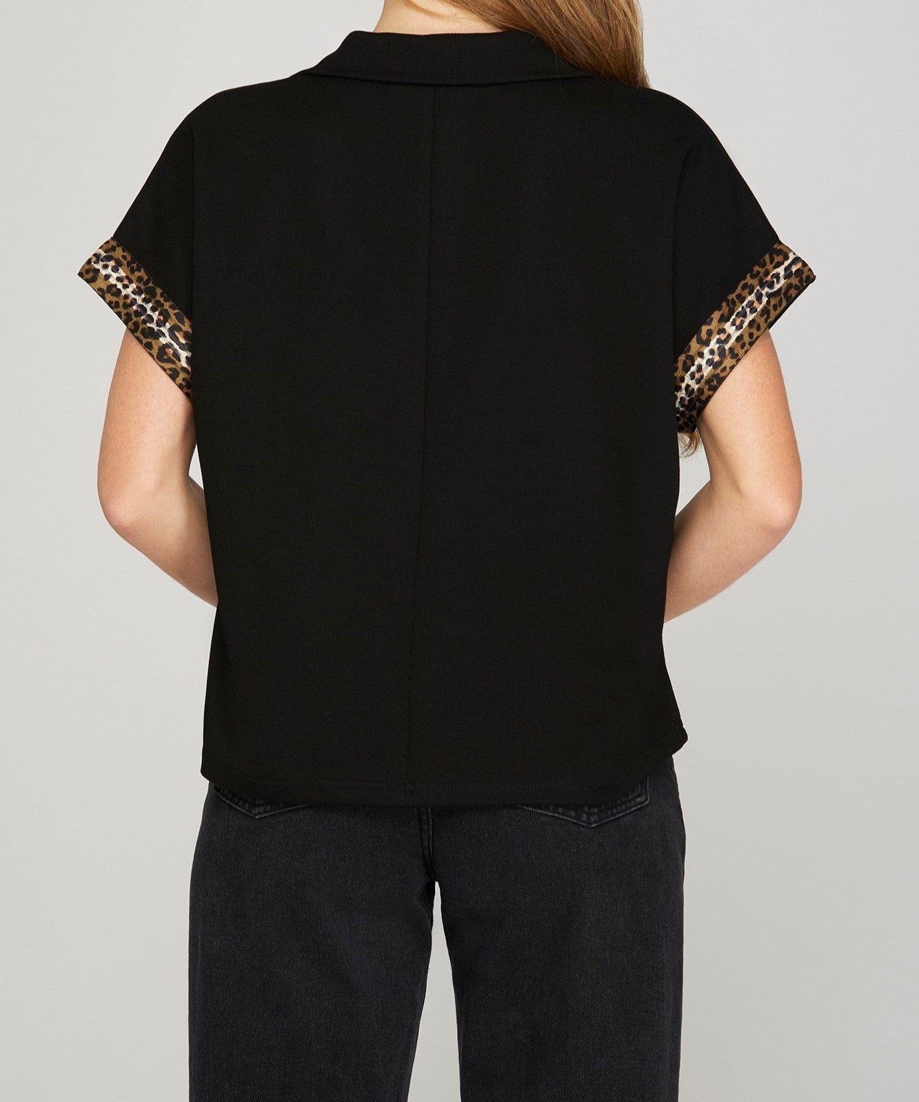 Back view of black shirt with leopard print sleeve stripes worn by a person on a plain background